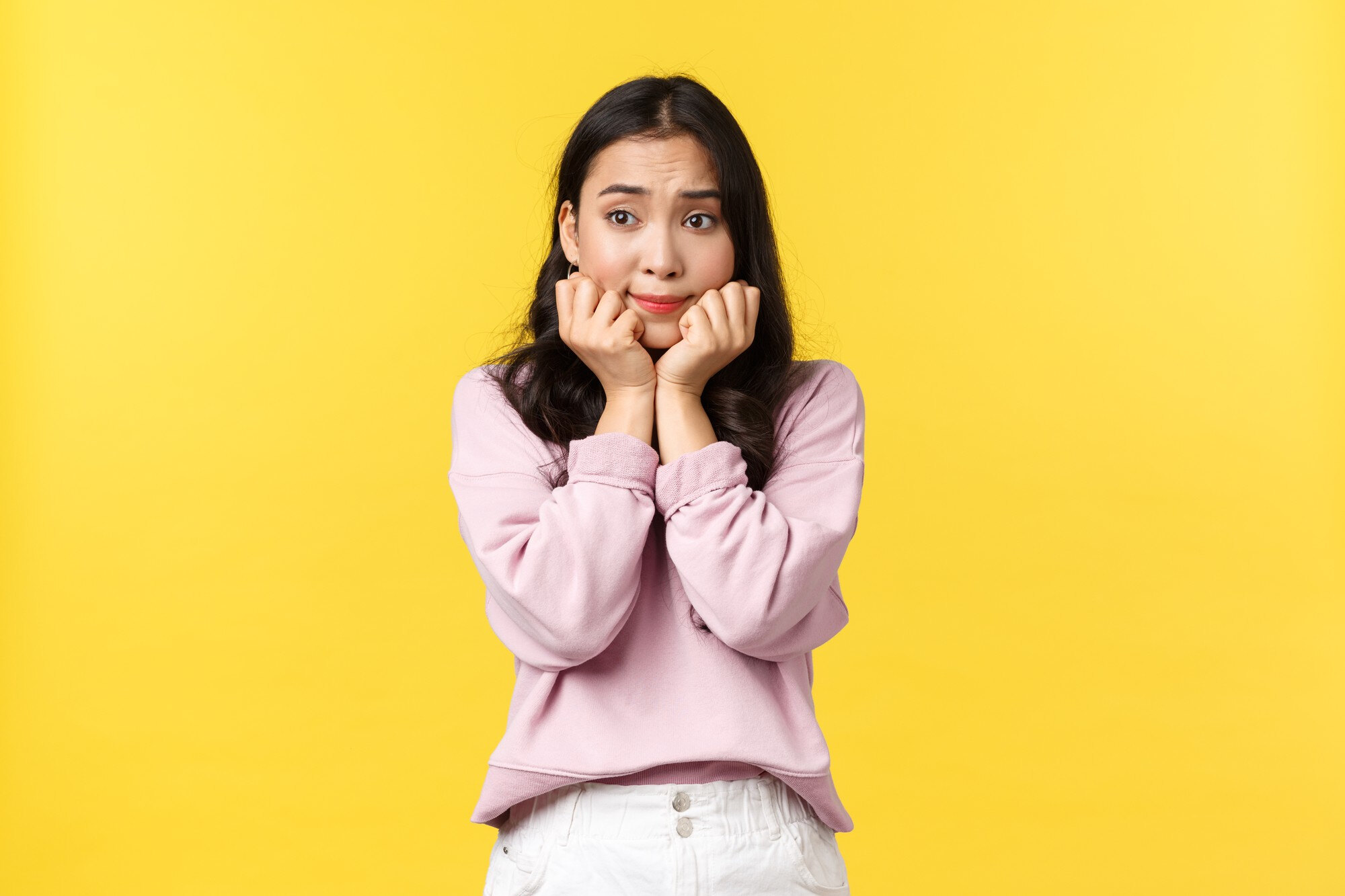  A young woman in a pink sweater and white jeans looks scared with her hands on her face, with the text "Tips mengatasi mimpi buruk bertemu nenek moyang" in Indonesian.